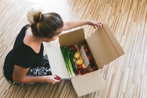 63947702 - woman opening a vegetable delivery box at home, online ordering